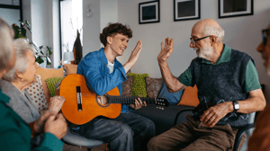 Young musician volunteer with guitar giving high five to senior man.