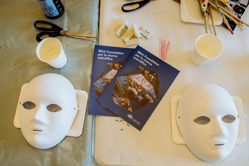 White masks and IBSA brochures on a table with creative workshop materials.