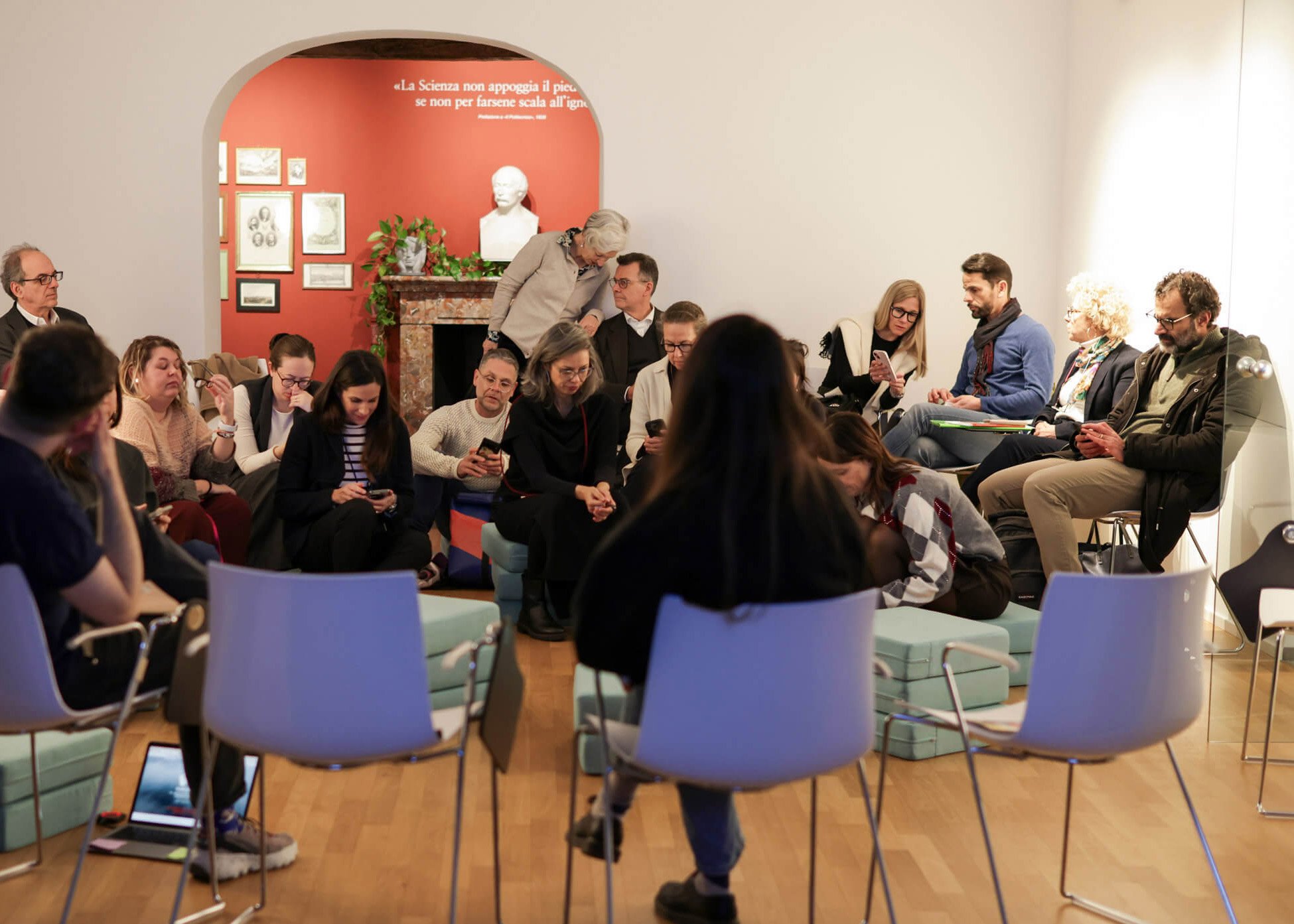 Partecipanti seduti in cerchio prendono appunti e ascoltano l’incontro in una sala di Casa Carlo Cattaneo, con il camino storico e le immagini alle pareti sullo sfondo.