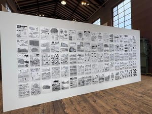 Wall exhibition of black-and-white comic illustrations displayed in a grid inside a spacious industrial gallery.