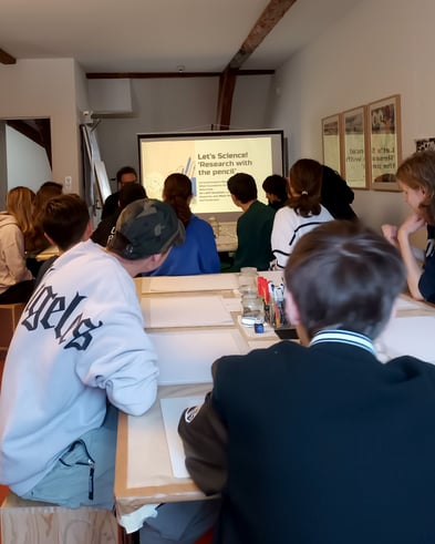 Studierende sitzen im Klassenzimmer und verfolgen eine einführende Präsentation zu einem Workshop über die Beziehung zwischen Wissenschaft und Kunst.