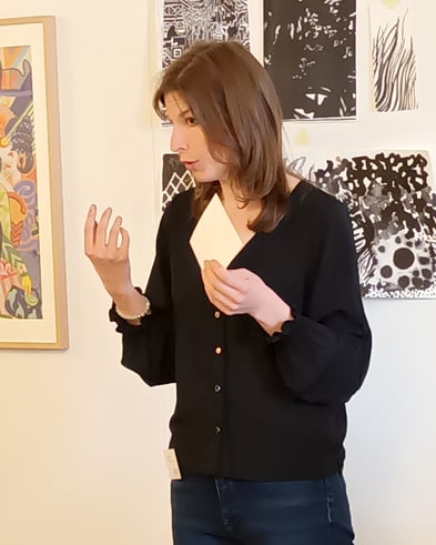 Eine Referentin präsentiert die künstlerische Aktivität vor einer Wand mit Werken und grafischen Experimenten.