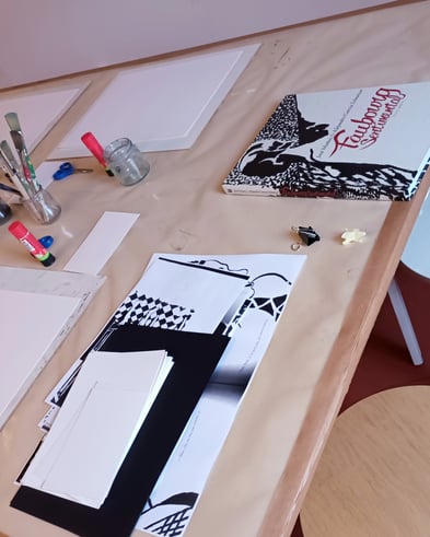 Ein Tisch, vorbereitet für einen Kunstworkshop, mit Papier, Pinseln, Zeichenmaterial und einem Bilderbuch.