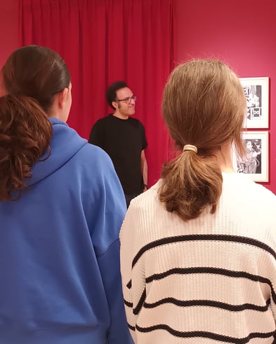 Studierende betrachten ausgestellte Werke, während ein Referent das Kunstprojekt vorstellt.