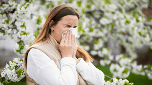 Sneezing woman with a nose wiper among the flowering trees in the park