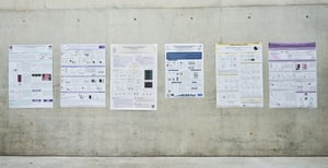 Poster scientifici affissi su una parete in cemento durante una sessione espositiva dedicata alla ricerca biomedica, con diversi contributi presentati nell'ambito di un congresso scientifico.