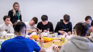 Gruppo di adolescenti seduti attorno a un tavolo mentre lavorano a un’attività creativa con maschere, colori e materiali artistici durante un laboratorio educativo.