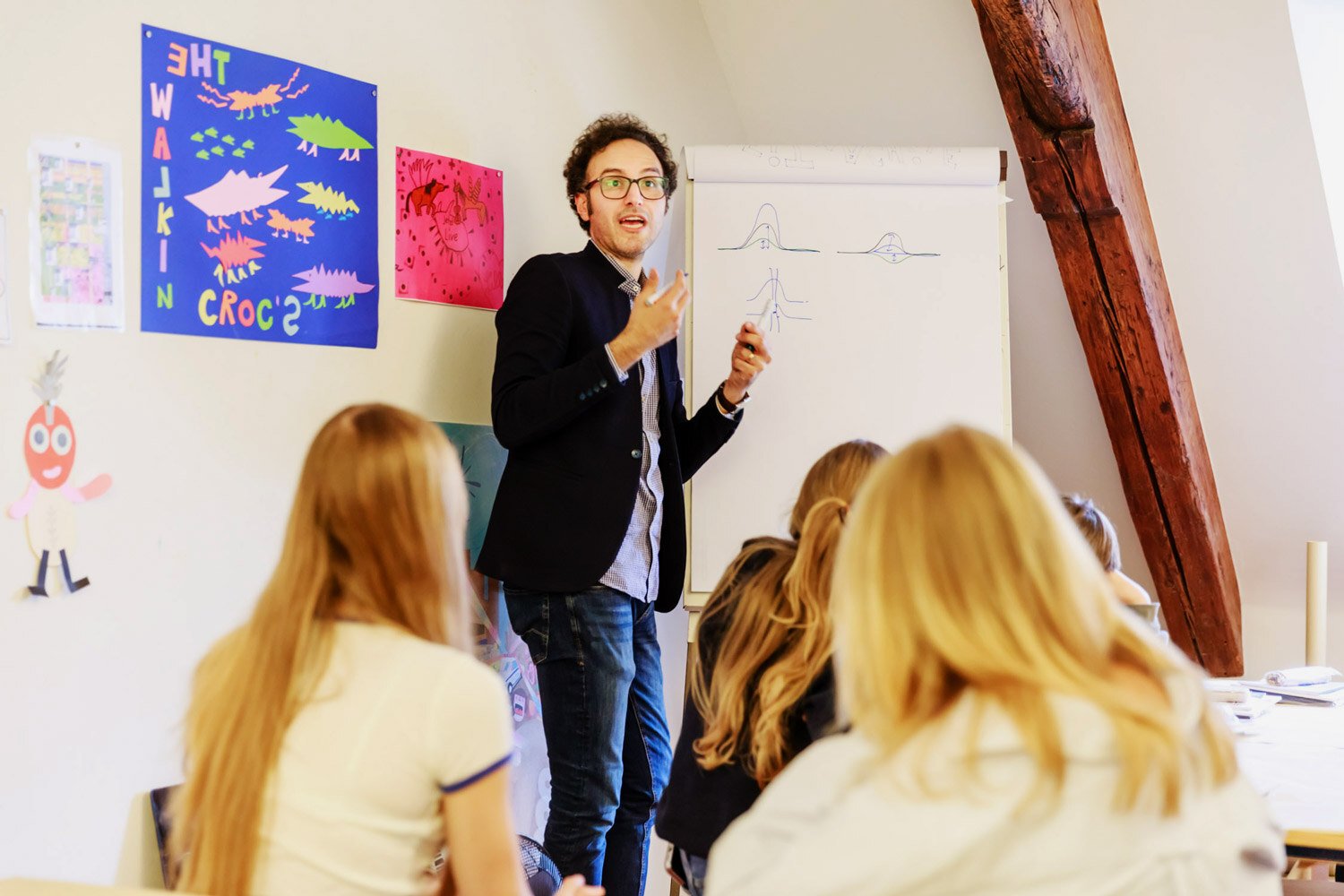 A physicist, with his back to a paper board, explains some concepts to an audience of students, photographed from behind. The man is holding a marker.