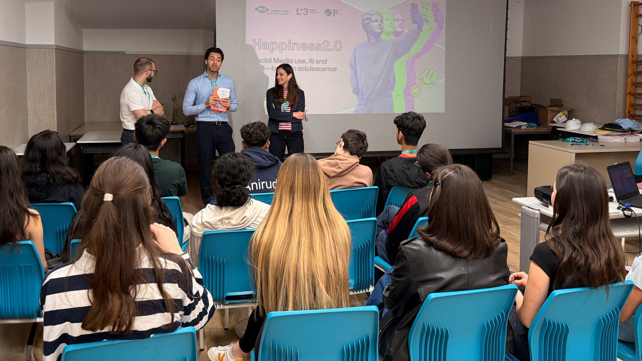 Tre facilitatori posano in aula con una maschera bianca e materiali pronti per il laboratorio HappyLab.