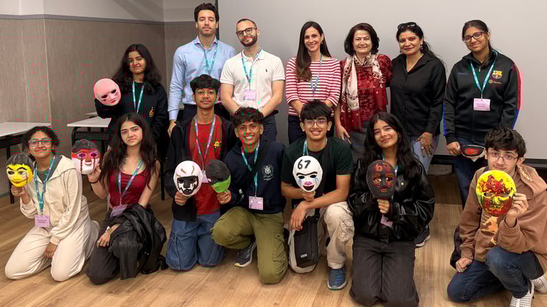 Gruppo di studenti e adulti durante un laboratorio HappyLab di IBSA Foundation, posano insieme mostrando maschere artistiche dipinte a mano in un’aula.