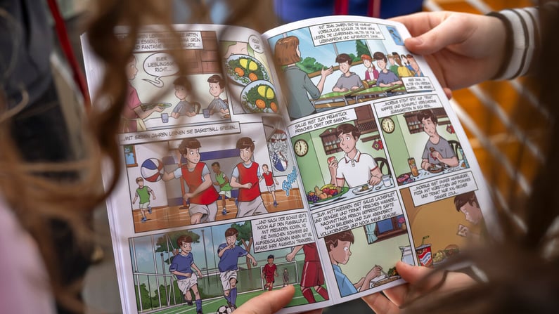 Close-up of children reading a colorful comic book about healthy habits and sports