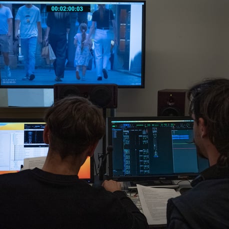 Due tecnici lavorano in una sala di montaggio audio e video, osservando su un grande schermo una scena del cortometraggio con timecode visibile.