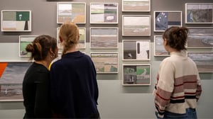 Drei junge Frauen betrachten eine Wand voller gerahmter Comic-Zeichnungen und Illustrationen in einer Ausstellung – eine Szene aus dem Projekt Let's Science! im Cartoonmuseum Basel.